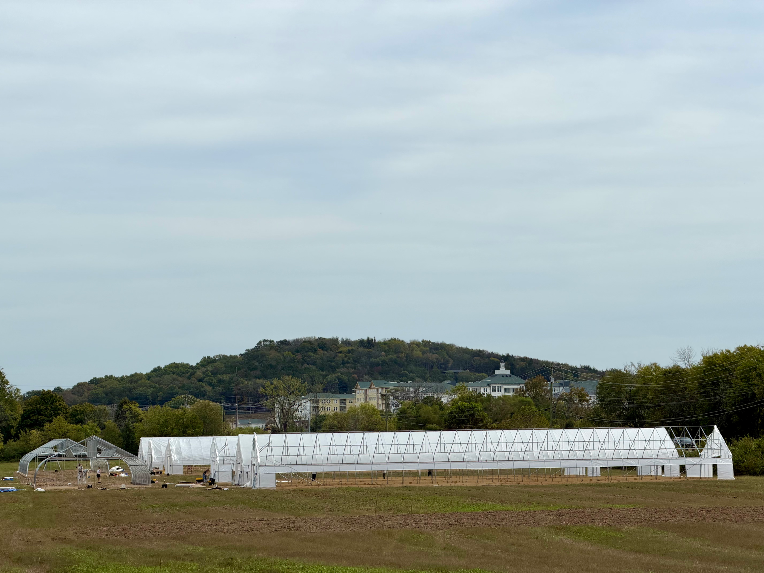 A wide view across the field shows covered high tunnels and remaining construction.