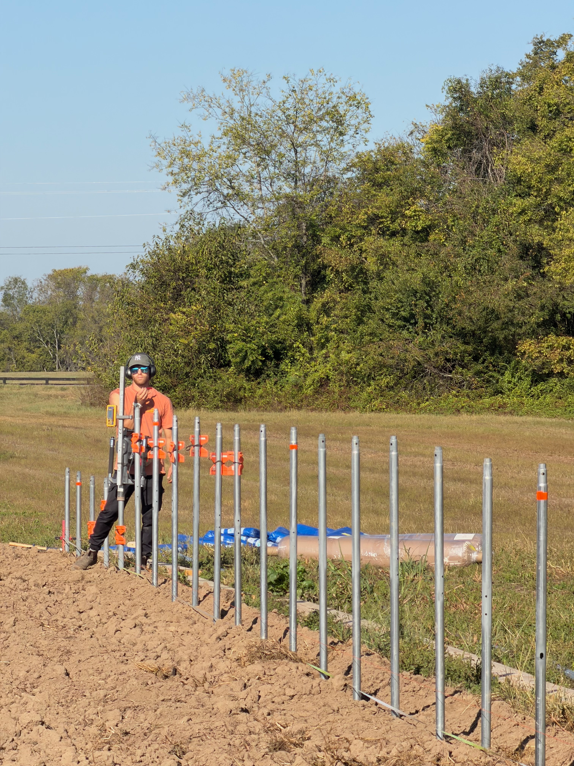 A worker stands beside a row of metal ground posts and clamps at the build site.