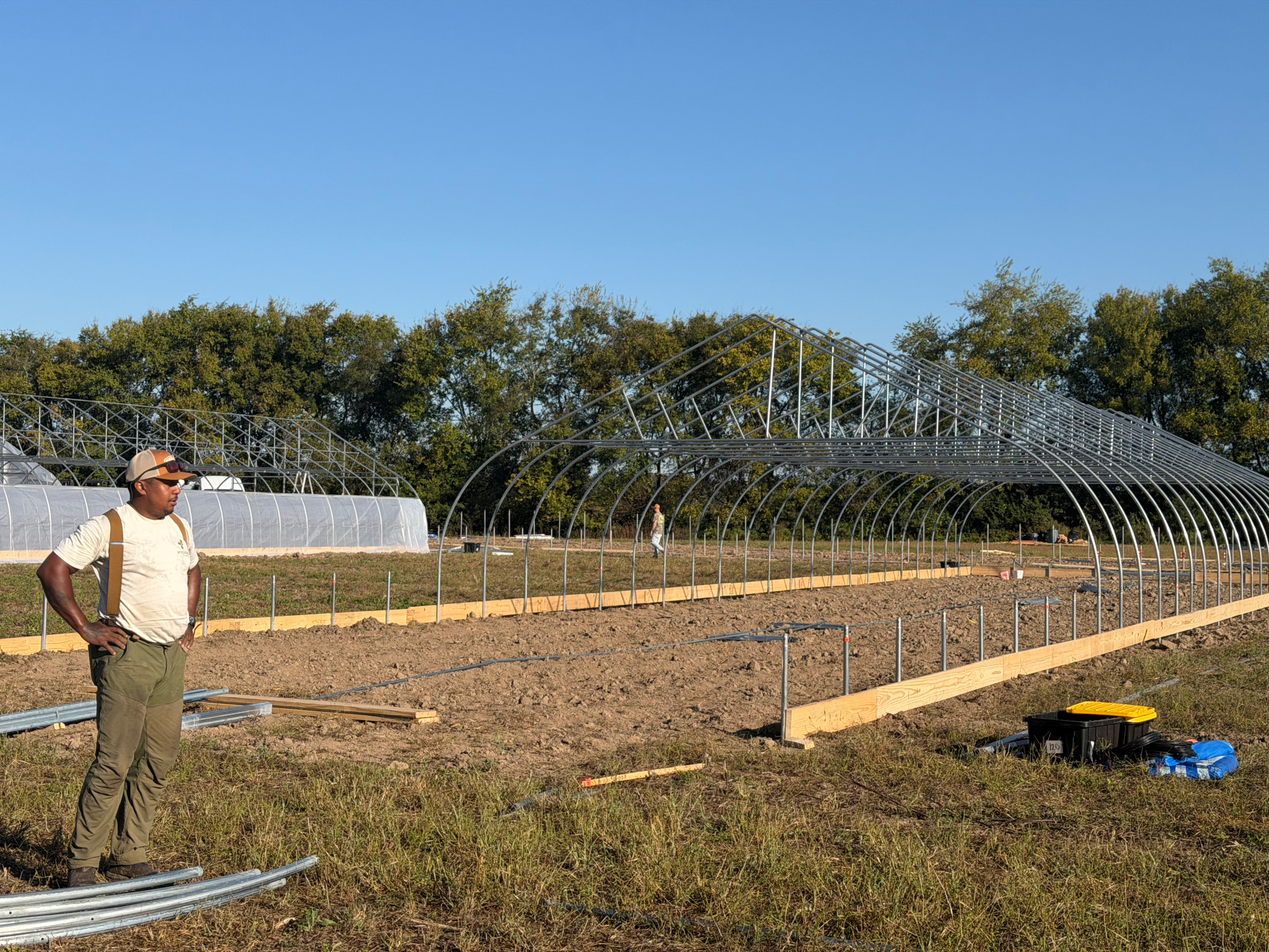 A worker stands beside uncovered hoop house frames at Armistead Farm.