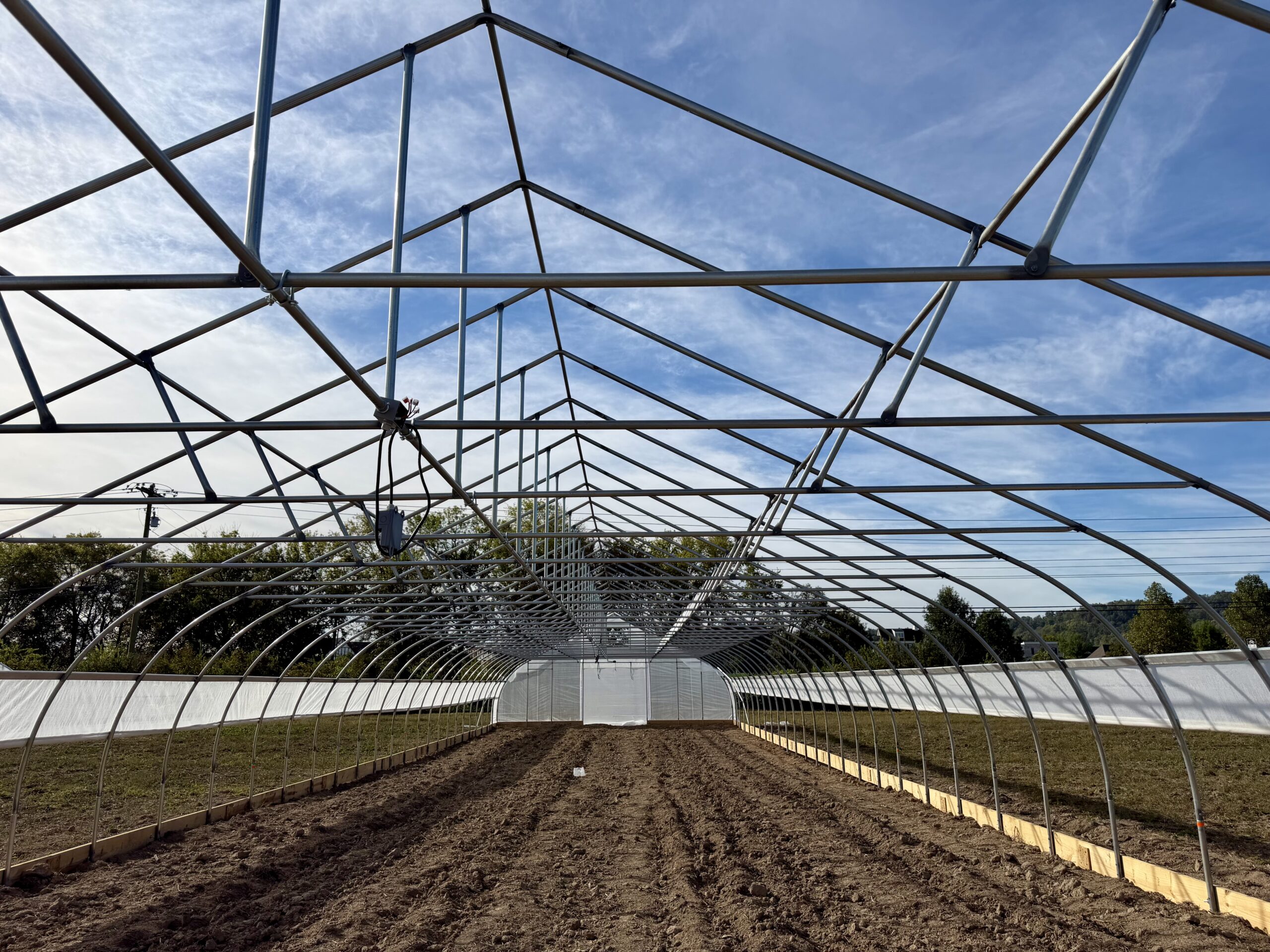 Uncovered metal arches and roof braces extend over prepared soil at Armistead Farm.